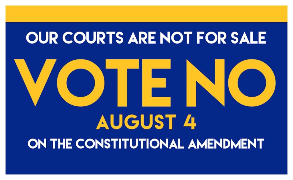 blue sign with white and yellow text that reads our courts are not for sale, vote no august 4 on the constitutional amendment